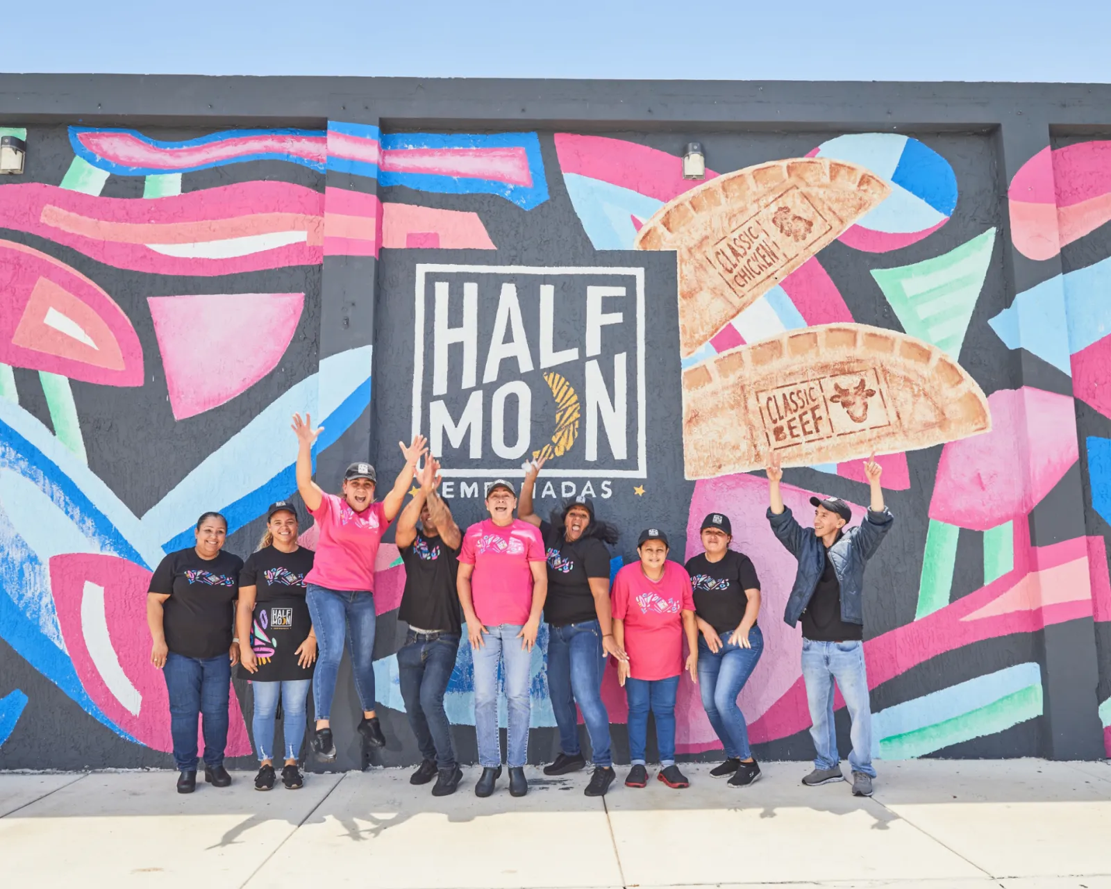 Half Moon Empanadas team in front of brand mural